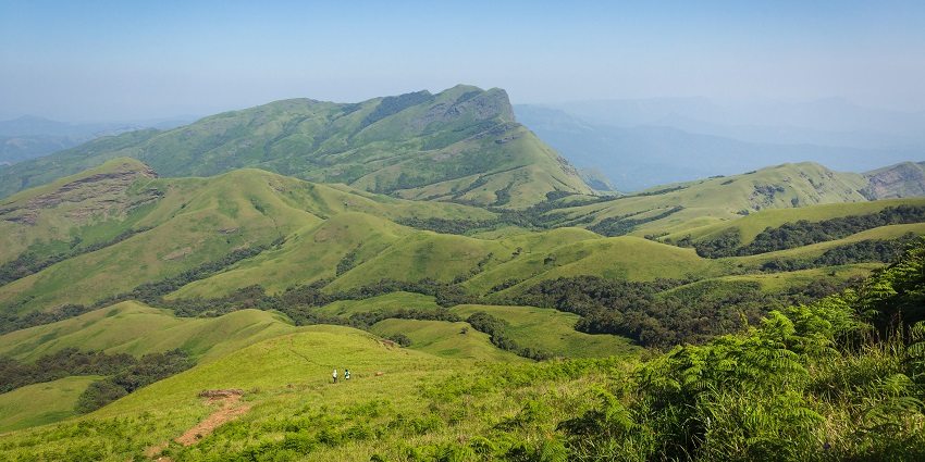 A stunning scenic view from atop a mountain with mist sweeping over green, rolling hills, one of the places for trekking in Karnataka.