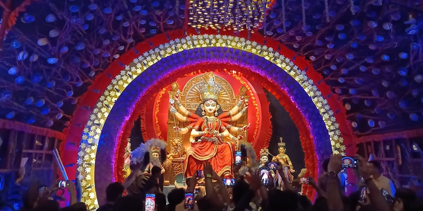 Crowd admires grand Durga idol in vibrant, illuminated Kumartuli Park Durga Puja pandal during Durga Puja in Kolkata.