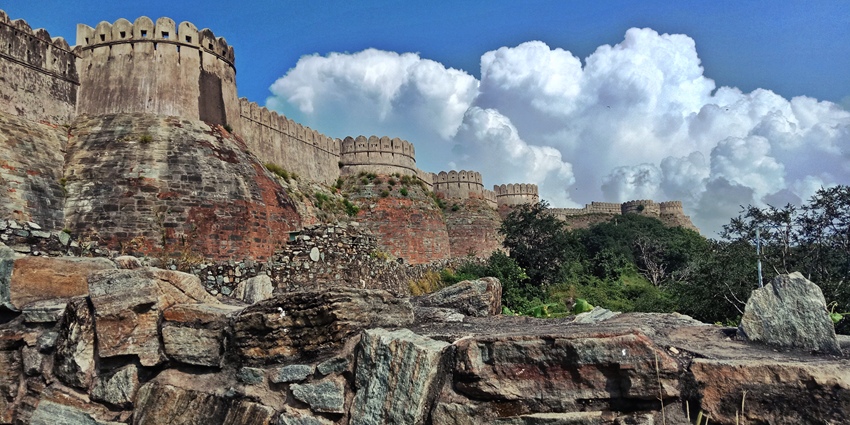 A massive stone fort wall with rounded towers winds across a rocky hill under a blue, cloudy sky.