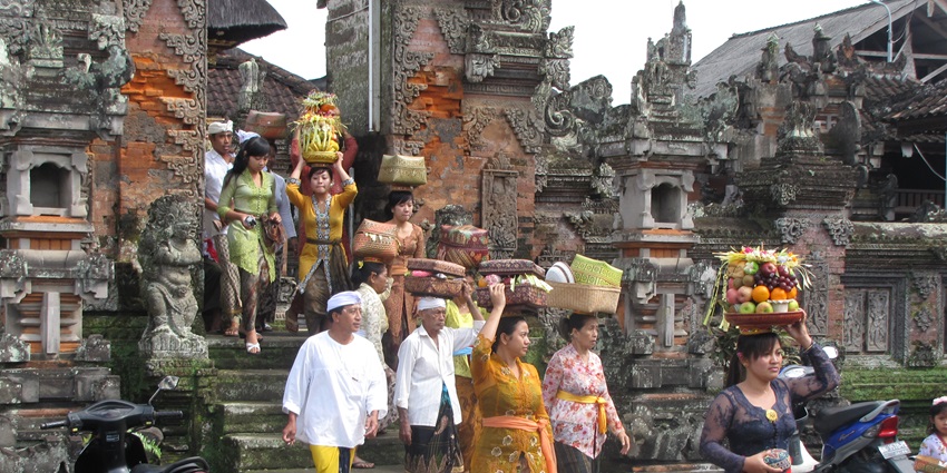 Women in traditional dress carry fruit offerings on their heads during a Balinese temple ritual.
