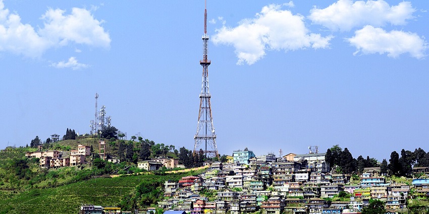 Kurseong town with a tall network tower, vibrant buildings & houses and green trees.