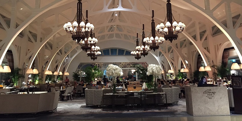 Elegant dining hall at The Clifford Pier with high arches and grand chandeliers lit
