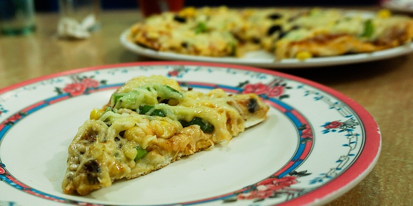 The thin-crust pizza is filled with veggies like capsicum, baby corn, and cheese.
