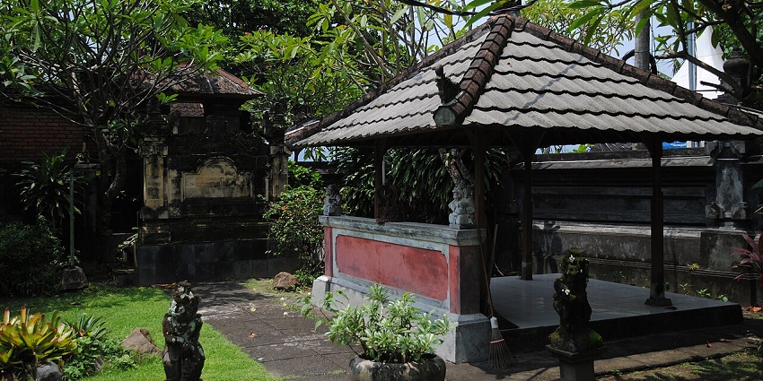 Traditional Balinese pavilion with tiled roof, stone statues, and lush garden setting.

