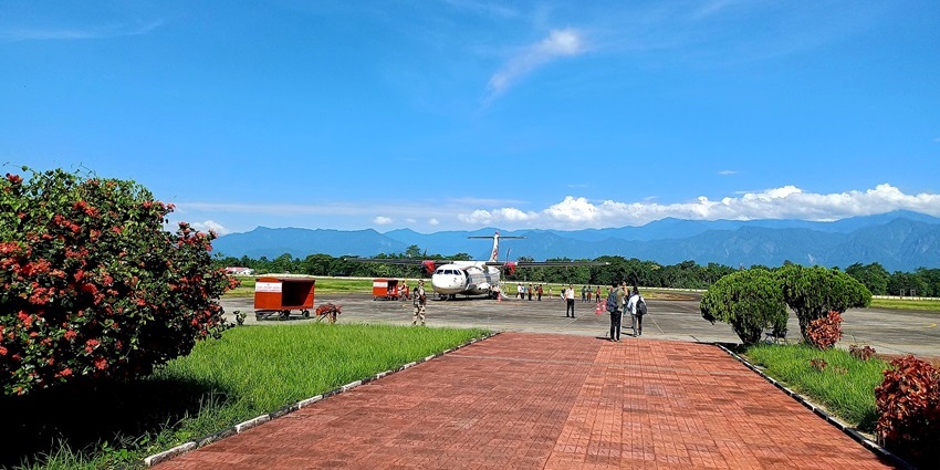 View of Lilabari Airport runway with passengers walking, aircraft parked, and hills in the backdrop.
