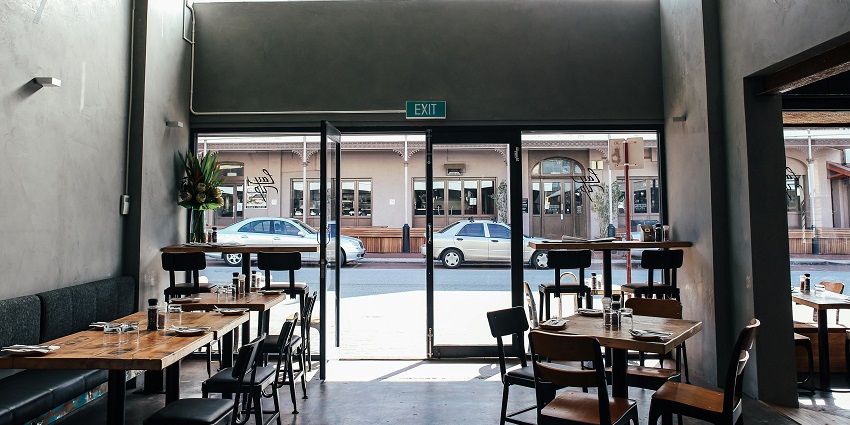 Wooden tables and black chairs arranged neatly near a wide glass door facing the street
