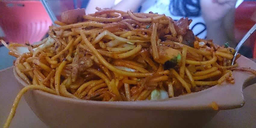 A large bowl of savoury noodles, mixed with meat and vegetables, ready to be enjoyed.
