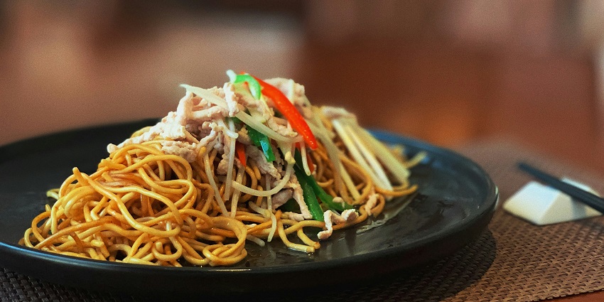 Noodles served on a black plate at a restaurant table in Mamagoto Restaurant.
