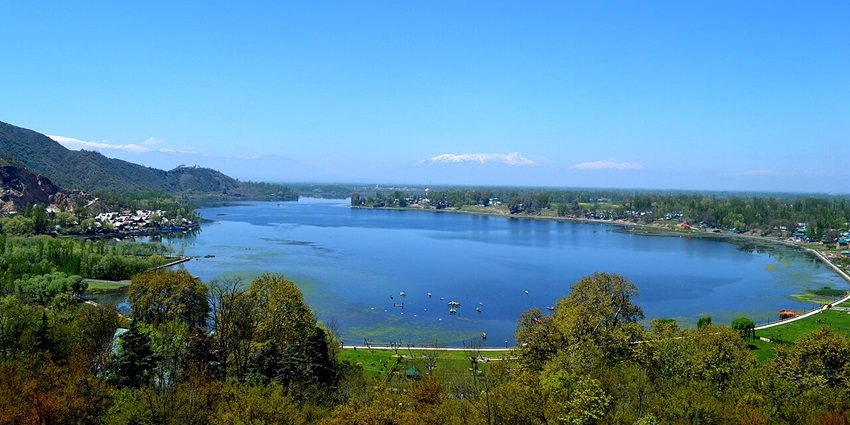 Large blue lake with trees and snow-capped mountains in distance, one of the top picnic places in Kashmir.