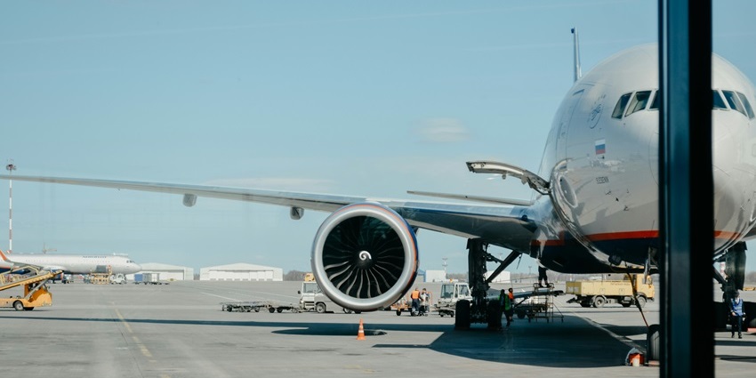 A large airplane parked at the Mangaluru International Airport gate with ground crew and service vehicles nearby.