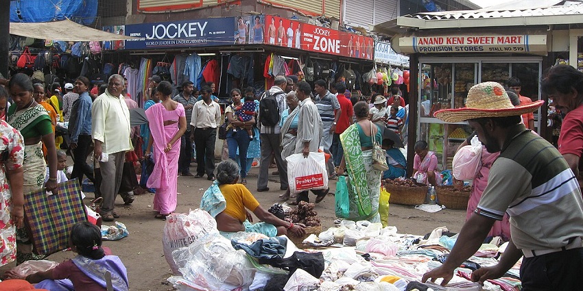 A busy outdoor market scene with many people and various street vendors and buildings.