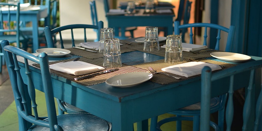 Sunlit table with blue chairs set for dining, plates and glasses neatly arranged
