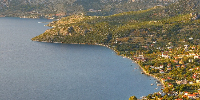 An elevated view of a coastal town with red-roofed houses surrounded by mountains.
