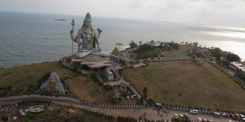 A wide shot of a large statue of a deity overlooking a body of water under a cloudy sky.