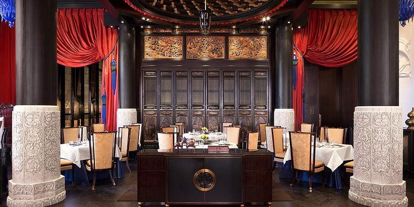 A formal dining room with red curtains, white tablecloths, and ornate wall carvings.
