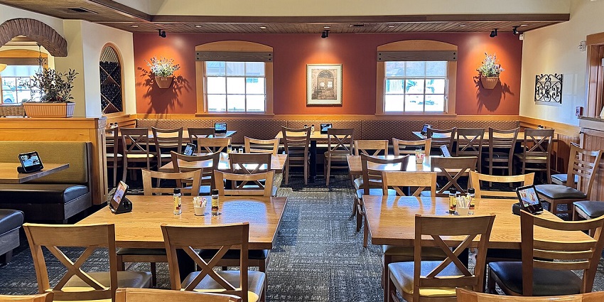 A well-lit restaurant dining room with many wooden tables and chairs, and booths.
