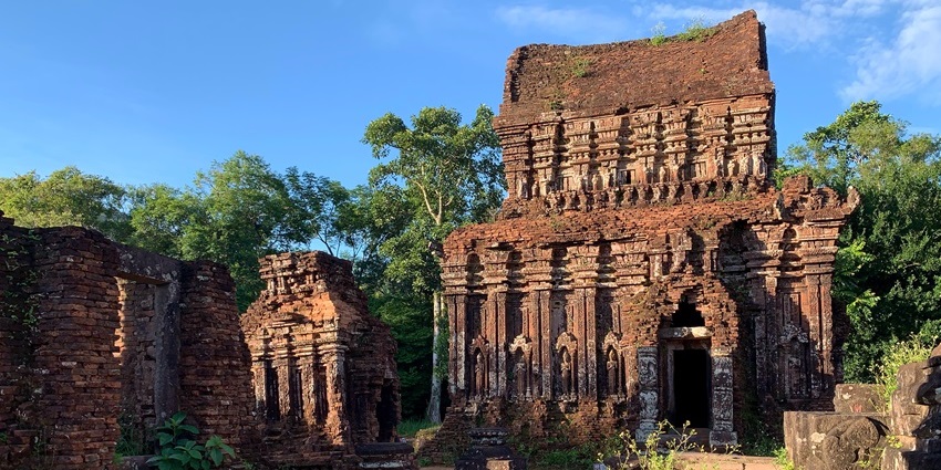 Ruins of My Son Sanctuary in Vietnam, with red-brick Cham temples partly covered in grass.