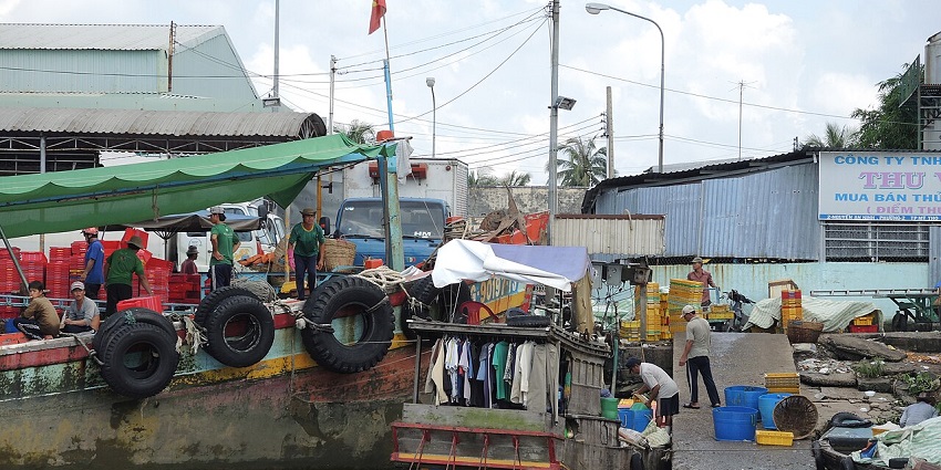 A group of people unload a large cargo boat docked on a river next to a dirt bank.
