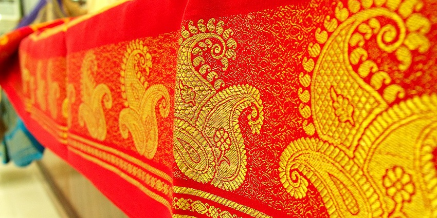 Close-up of bright red material with detailed gold paisley prints, classic saree.
