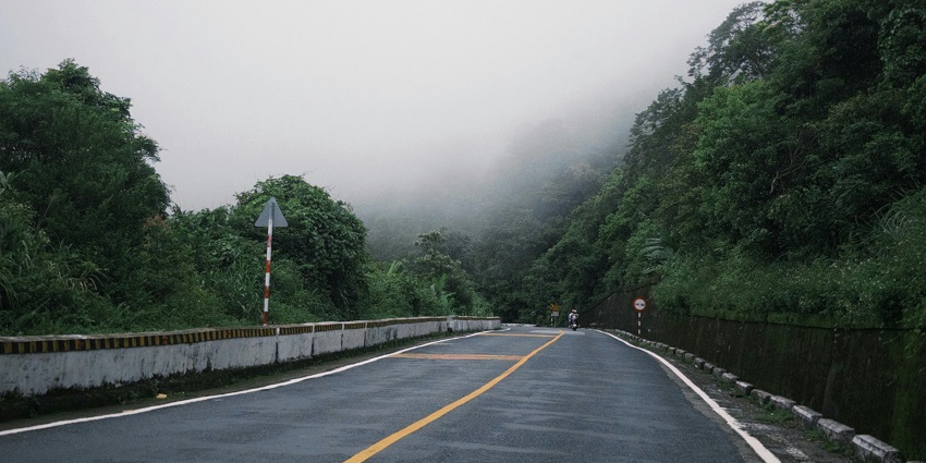 Foggy road cutting through lush green trees and vegetation along NH4 Highway.