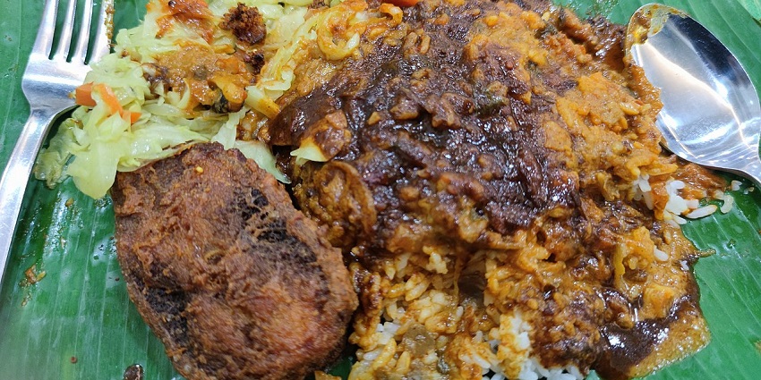 A plate of delicious rice with rich curry, a fried cutlet, and vegetable toppings.

