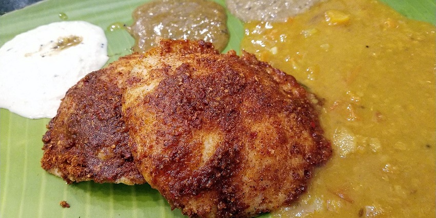 Two crispy, fried idlis served on a banana leaf with three different dipping sauces.
