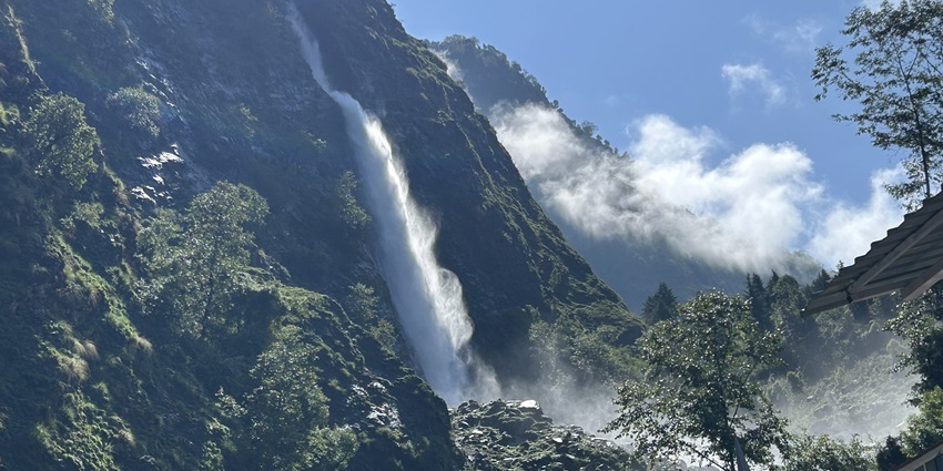 A tall waterfall cascading down a steep rocky mountain, surrounded by trees and misty clouds.