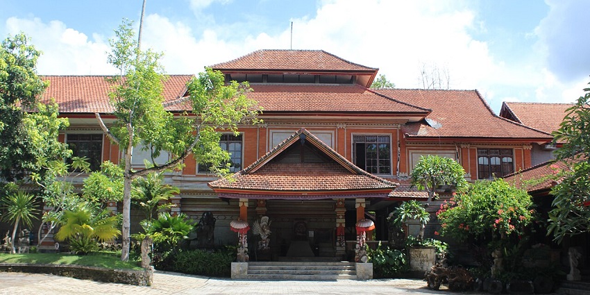 Front view of Neka Art Museum in Ubud with red-tiled roofs, trees, and a stone courtyard.
