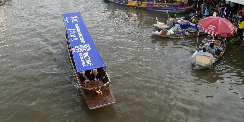 A large crowd of boats on a river, with some docked along the shore where vendors are.
