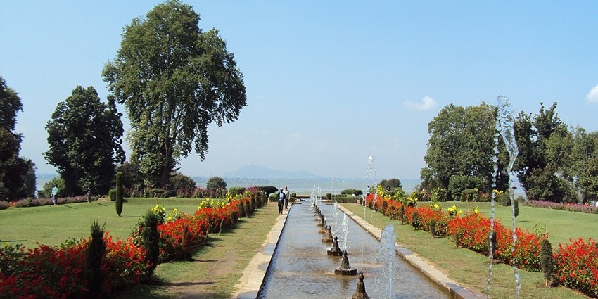 A formal garden with a long canal of fountains flanked by rows of red and yellow flowers.