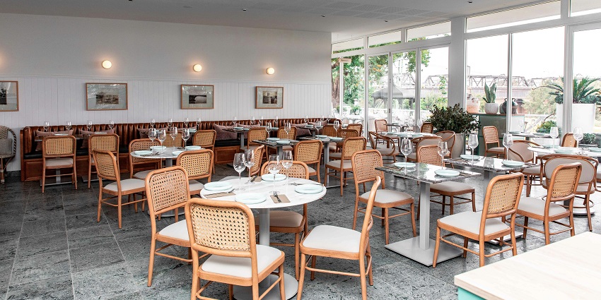 Elegant restaurant interior with natural light, rattan chairs, and well-arranged glassware, one of the best restaurants in Clarke Quay.
