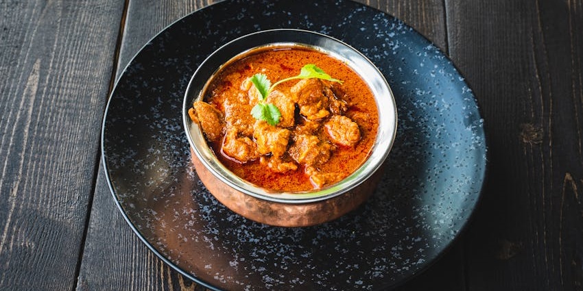 Close-up of a bowl of butter chicken curry garnished with fresh coriander leaves, served at Paankhuri Restaurant.