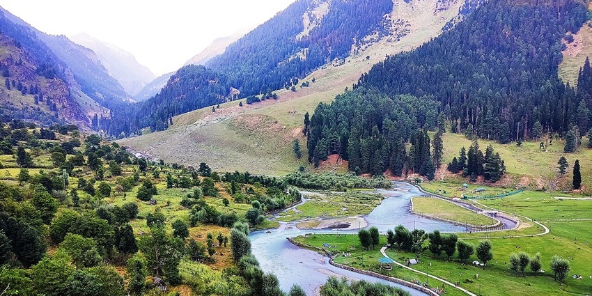A long river winds through a lush green valley with scattered trees and a steep mountain slope.