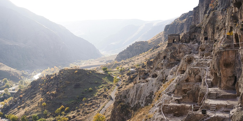 A scenic view of Patal Bhuvaneshwar Cave with ancient ruins in rocky valley landscape.
