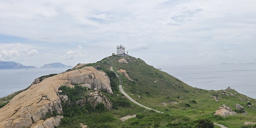Po Toi Island lighthouse on a green cliff with steps leading upward in islands in Hong Kong.