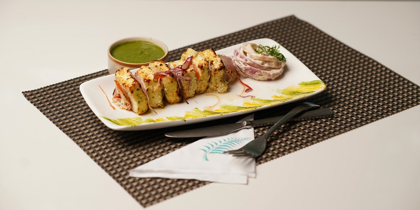 Plate of paneer tikka with vegetables and chutney served at a restaurant table.
