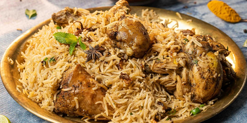 A gold platter is piled high with a fragrant chicken biryani with chicken pieces and spices.
