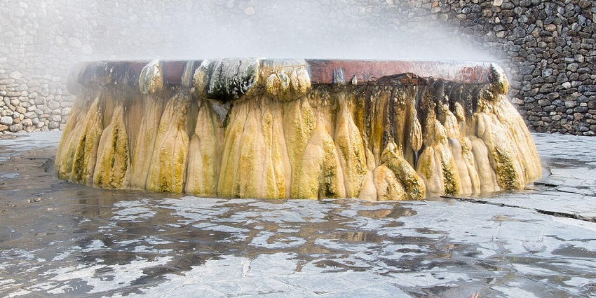 Steaming geyser hot spring at Raksawarin Park in Ranong with mineral deposits and a stone wall.