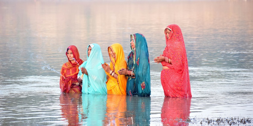 People are praying to the sun god during the sunrise while dipping in the water during Chhath Puja.