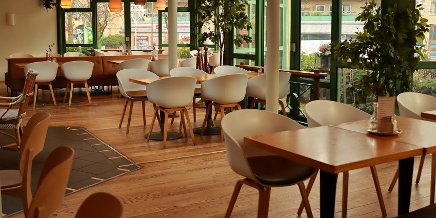 Modern restaurant with white chairs, wooden tables, large windows, and warm hanging lamps
