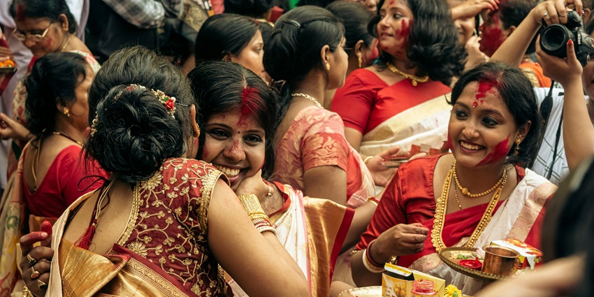 Women in traditional Bengali sarees celebrating Sindoor Khela by applying vermilion to each other.
