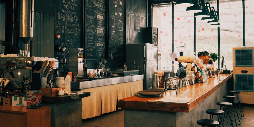 Minimalist café with baristas at the counter, concrete walls, plants and simple wooden décor
