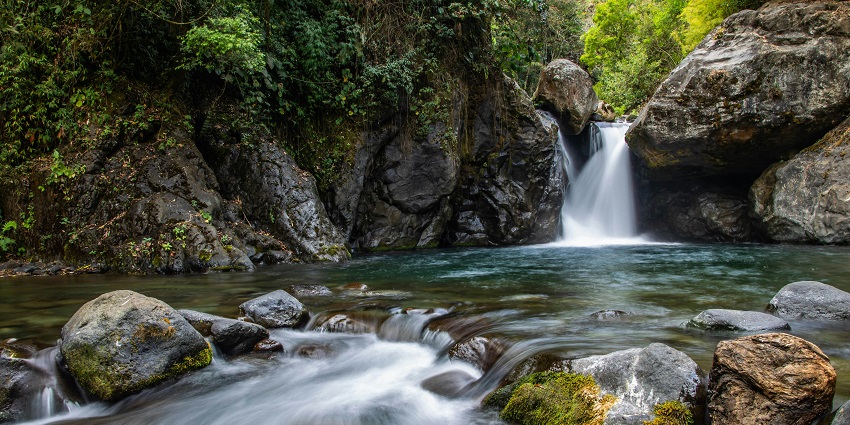 Sada Waterfall cascading over rocks, surrounded by lush greenery and natural beauty.
