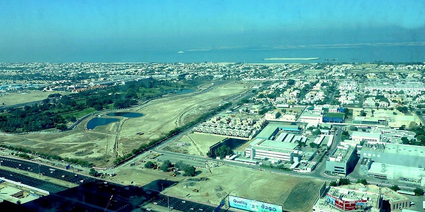 Green lawns and tall trees in a spacious park under a clear, bright sky with open views.
