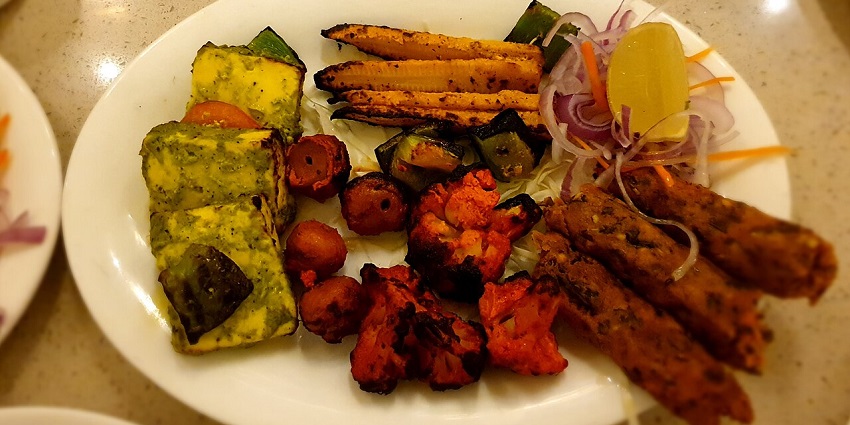 A plate full of veg starters like paneer tandoori, baby corn fry, salads, and soya chap.