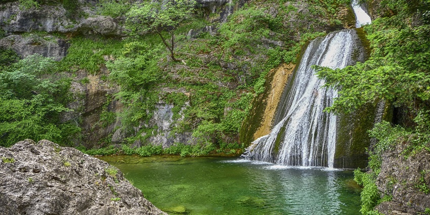 Small cascading stream flowing over rocks and stone ledges, surrounded by boulders and greenery, one of the top waterfalls in Uttarakhand.