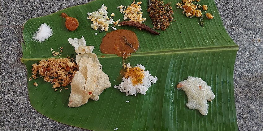 A variety of food is served on a banana leaf, including rice, curries, and fried snacks.
