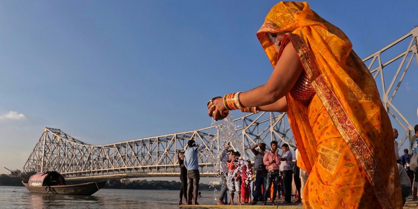 A woman in traditional attire standing in the water offering arghya to the Sun God during sandhya arghya.