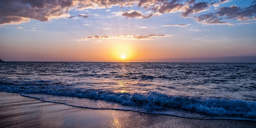 Sunset view of a sandy beach on Sanyasi Island with calm waters and palm trees.
