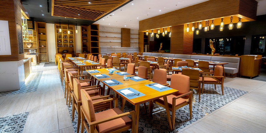 Modern restaurant with wooden ceiling panels, warm lighting, and neatly set dining tables
